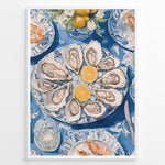 Ladda upp bild till gallerivisning, Oyster platter art print plakat showing oysters and lemon slices on a blue patterned table with seafood dishes and glassware in a White frame.
