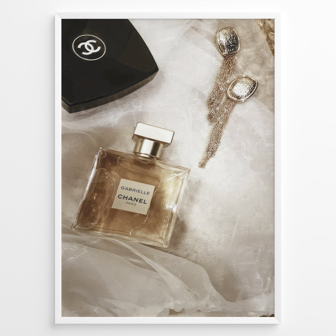 Fashion Plakat | Chanel Gabrielle Perfume Flat Lay with Earrings and Compact – Luxury Beauty Print Plakaty.dk | Flat lay image of Chanel Gabrielle perfume, a black Chanel compact, and gold statement earrings on soft white fabric.