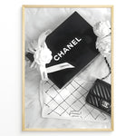 Ladda upp bild till gallerivisning, Fashion Plakat | Chanel Gift Box &amp; Handbag Flatlay Wall Art Plakaty.dk | Black and white flatlay of a Chanel gift box with ribbon, camellia flowers, and a quilted Chanel handbag on a soft surface.
