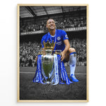 Ladda upp bild till gallerivisning, John Terry im Chelsea-Trikot mit der Premier-League-Trophäe vor den Chelsea-Fans. Die ikonischen blauen Farben heben sich vom schwarz-weißen Stadionhintergrund ab.

