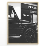 Ladda upp bild till gallerivisning, Fashion Plakat | Mercedes-Benz G-Wagon and Prada Store Black and White Art Print Plakaty.dk | A framed, black and white photograph showing the side profile of a Mercedes-Benz G-Wagon AMG parked in front of a Prada store. The car&#39;s V8 BITURBO badge is visible, and the Prada logo is prominent on the building&#39;s facade.
