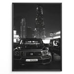 Ladda upp bild till gallerivisning, Fashion Plakat | Midnight Luxury – Brabus G-Wagon in Dubai Plakaty.dk | Black and white photo of a Brabus G-Wagon parked in front of the Dubai skyline at night, with skyscrapers like Burj Khalifa and EMAAR towers in the background.
