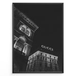 Ladda upp bild till gallerivisning, Fashion Plakat | Night View of Gucci Building Facade Plakaty.dk | Black and white nighttime photo of an ornate building with classical columns and arches next to a building displaying a large illuminated &quot;GUCCI&quot; sign against a dark sky.
